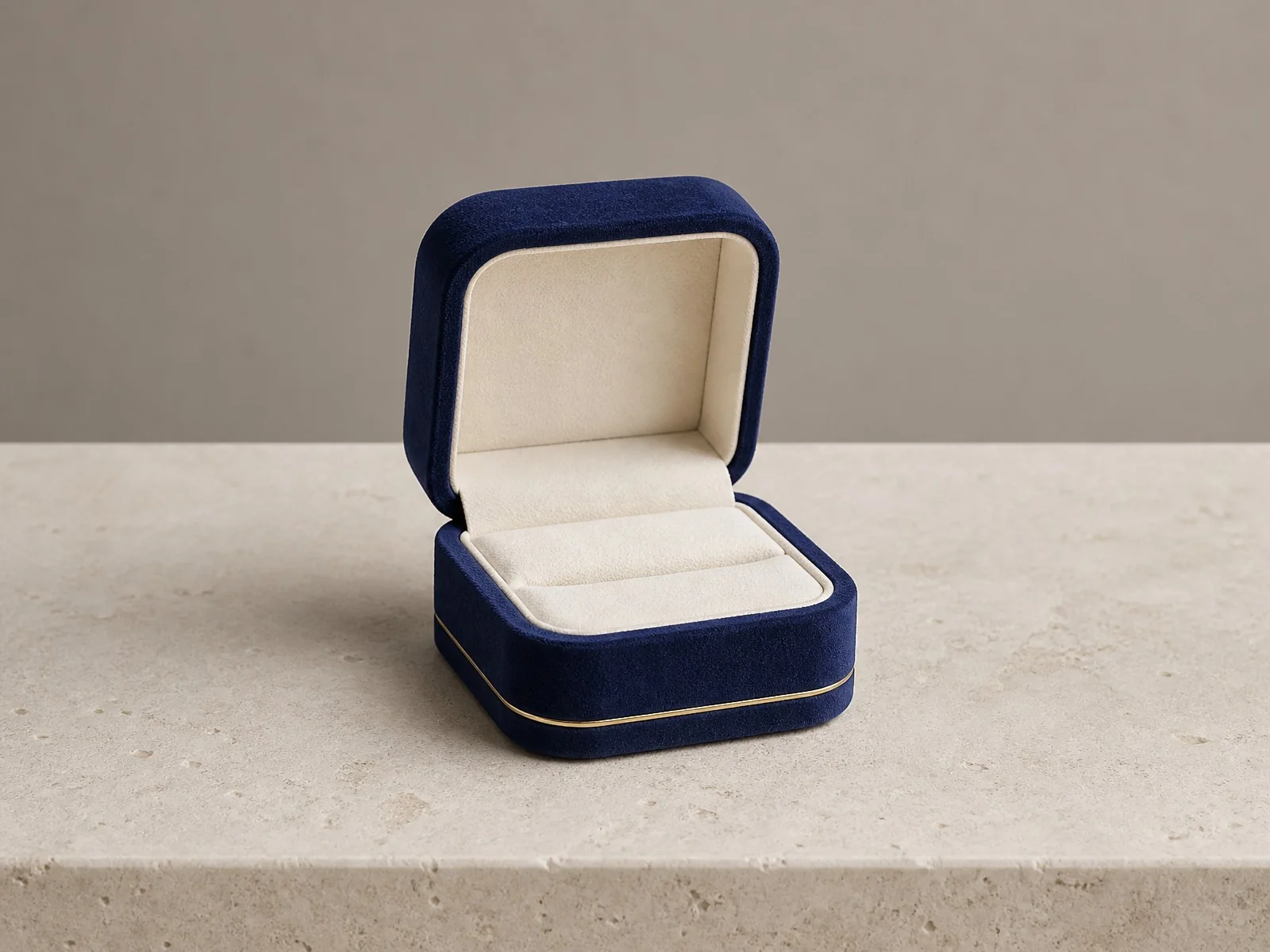 custom jewelry packaging cost series image one - navy velvet ring box with a cream insert and a single ring slot, on a travertine surface against a grey wall